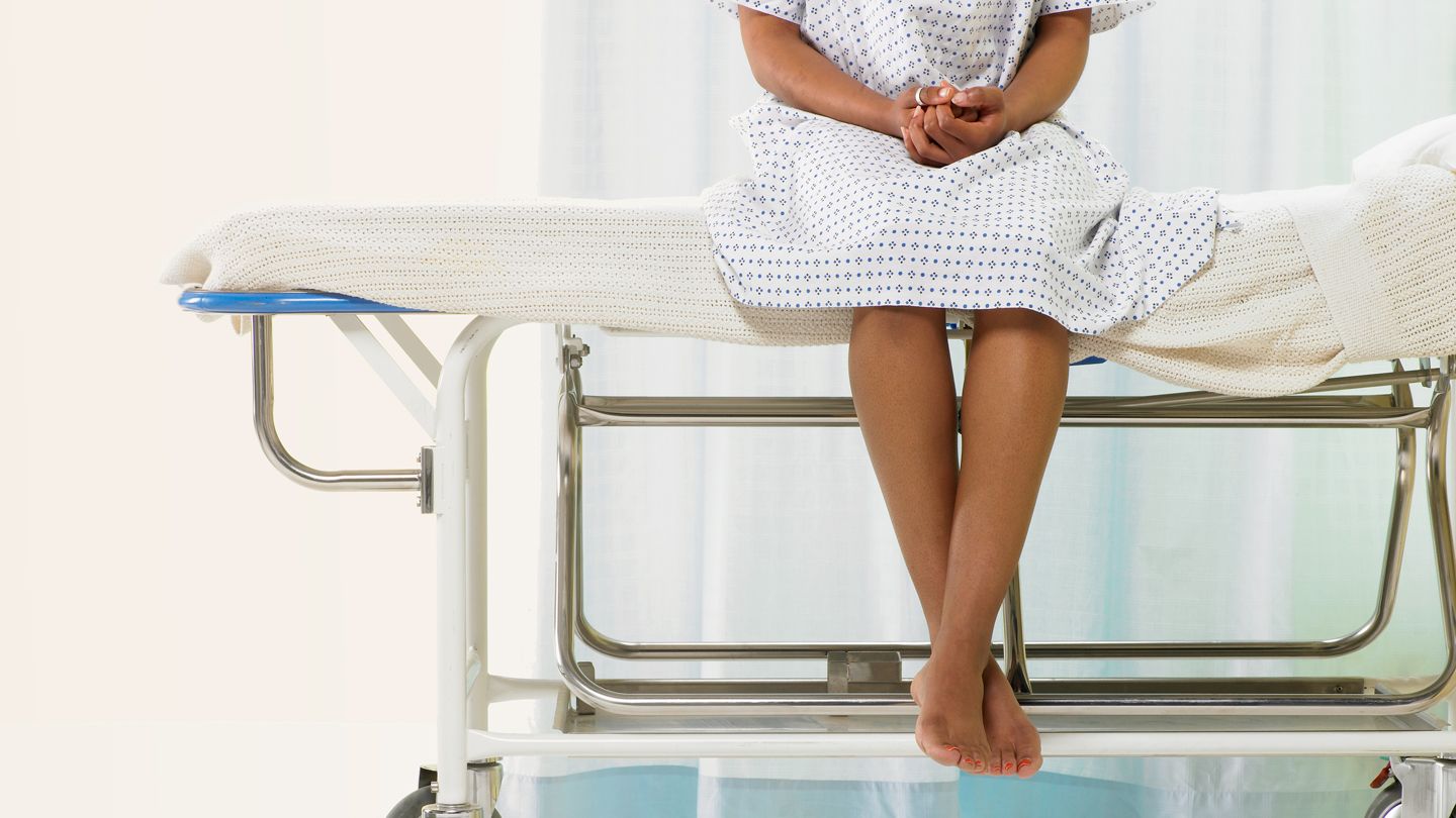 Black Female patient sitting on gurney in hospital gown