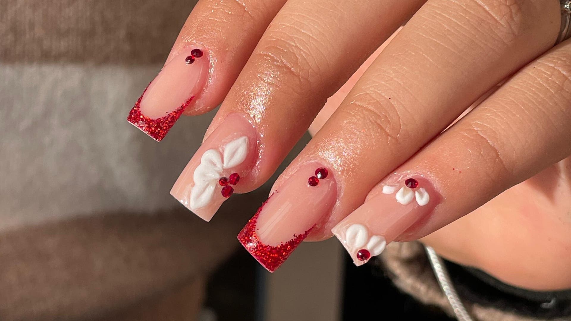 Uñas decoradas con glitter rojo y flores blancas en Lizeth Nails, Madrid, Comunidad De Madrid, ES.