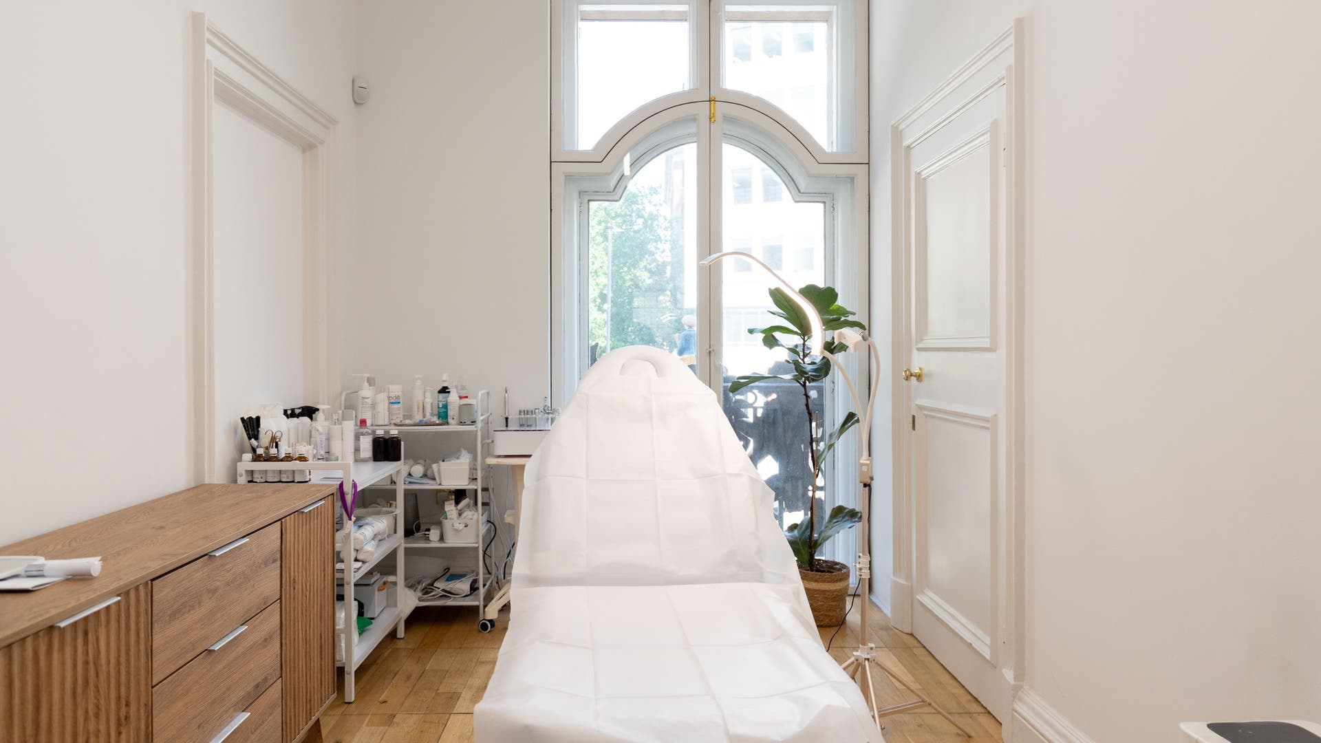 Bright, serene treatment room at MESOAETHETIC, London, England, GB featuring a cushioned chair and lush plant décor.
