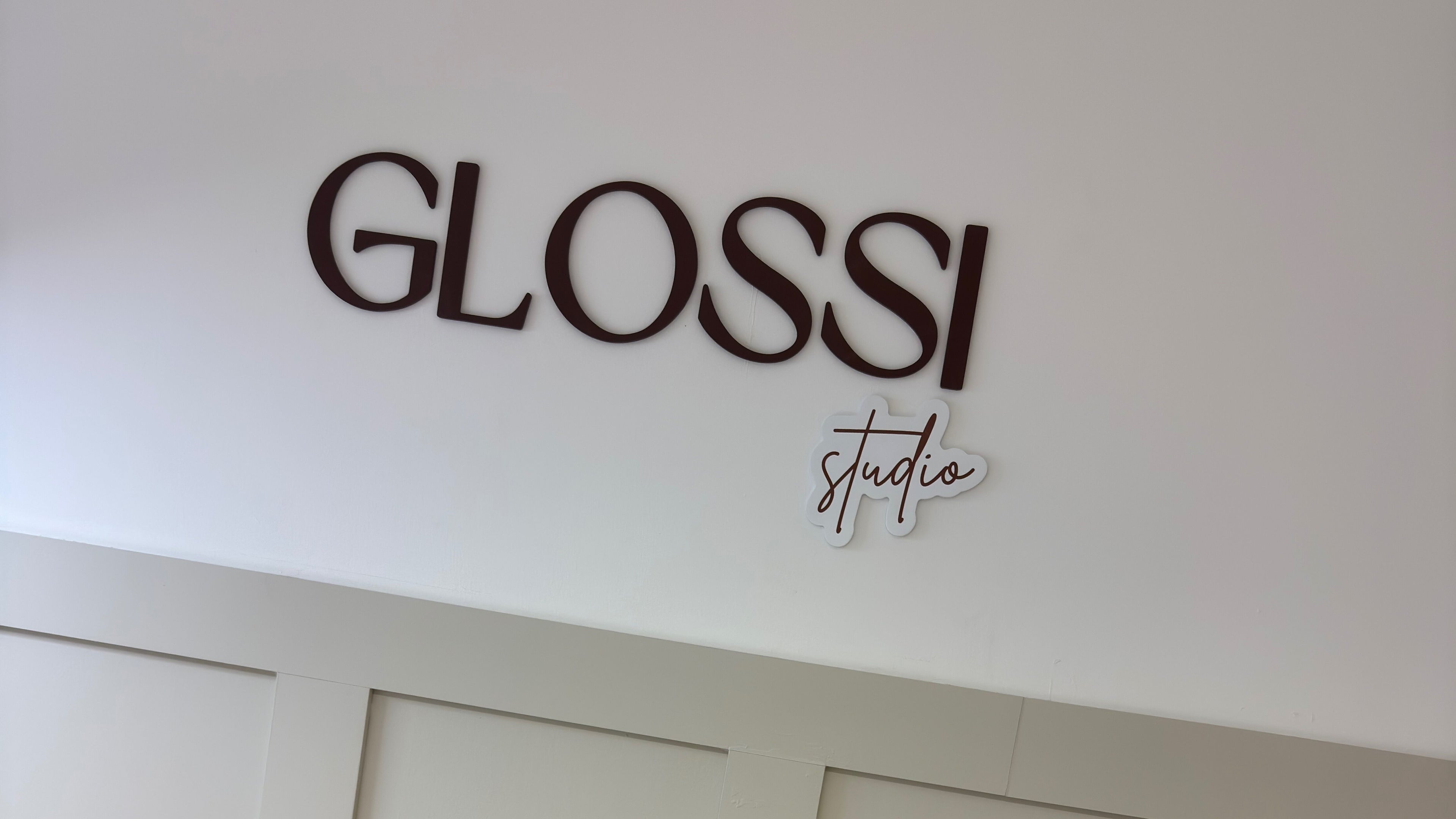 Glossi Studio signage on a white wall in Clydebank, Scotland, GB showcasing elegance.