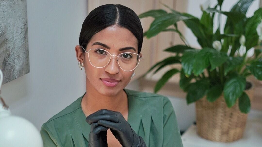 Profissional em Stefane Nails Bio, Lisboa, vestindo luvas pretas e camisa verde, com planta ao fundo.