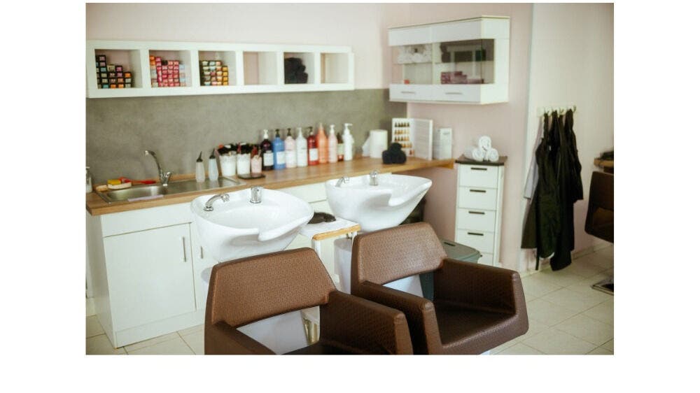 Elegant hair washing area at Hair by Tusha, Edmonton, Alberta, CA, featuring modern chairs and stocked shelves.