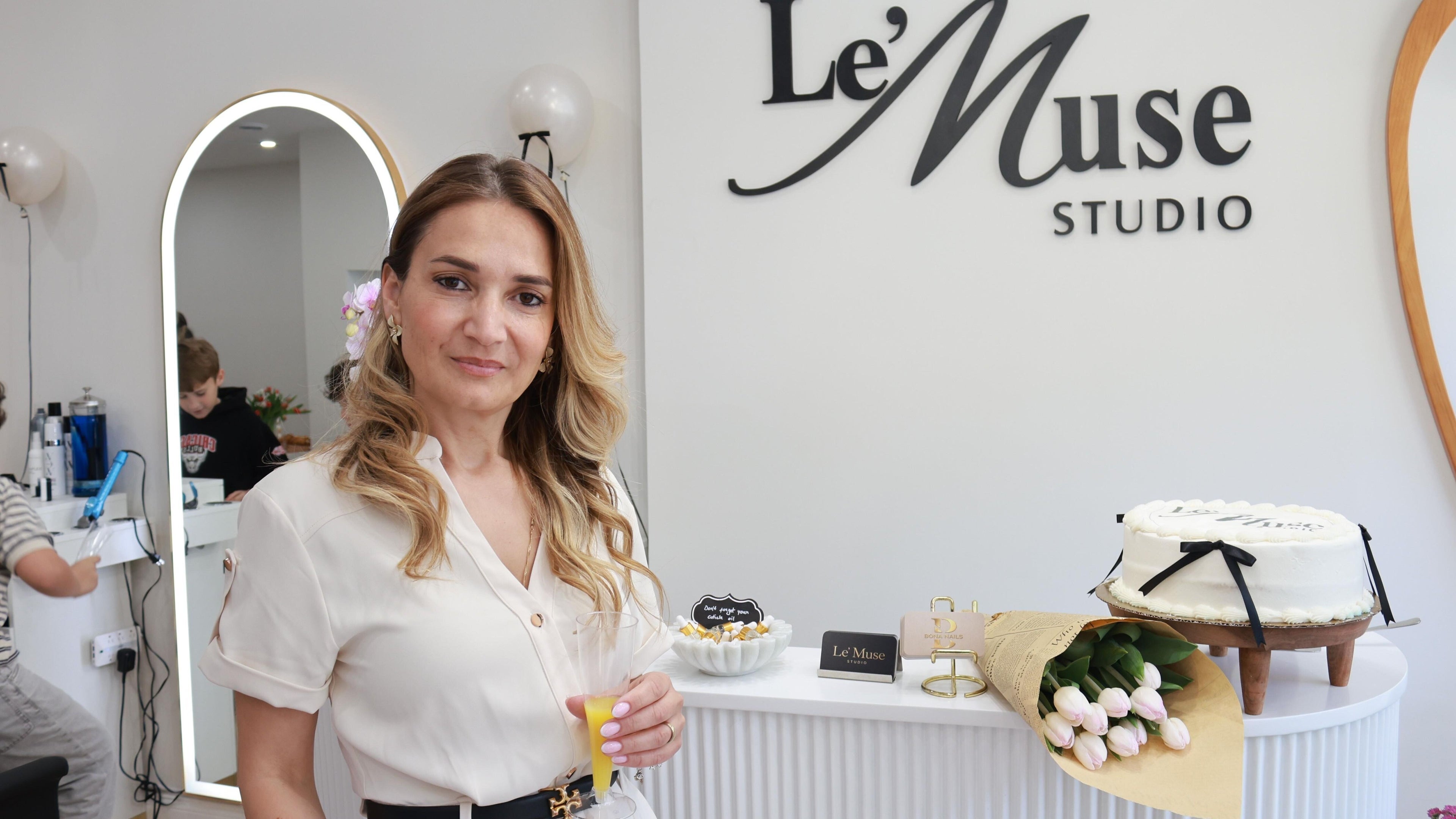 Woman at Le’Muse Studio in New York, New York, US, holding a drink with cake and tulips on the counter.