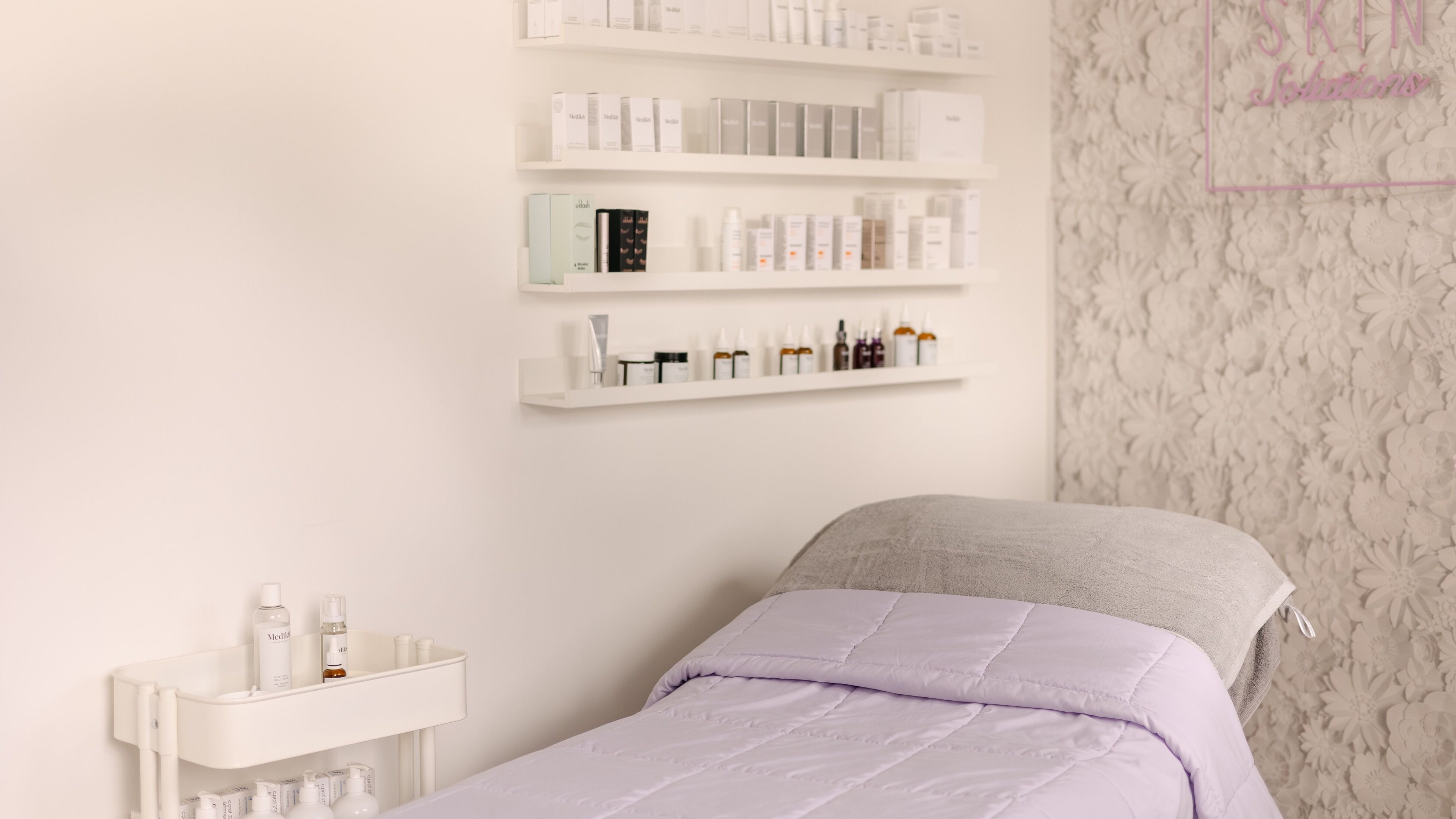 Tranquil treatment room at Skin Solutions in Church Crookham, England, GB with floral wall and skincare products.