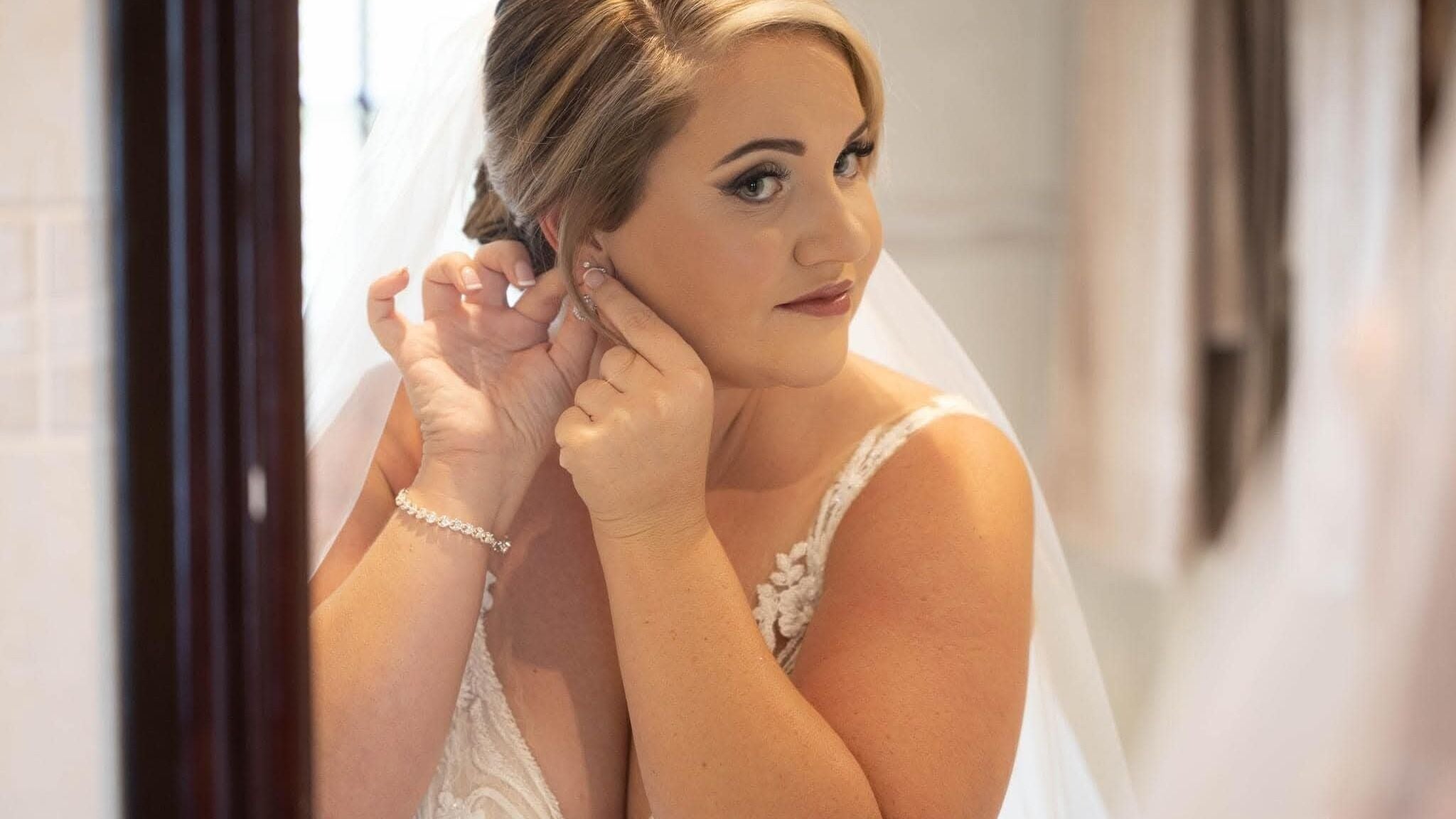Bridal makeup at Salon Styliqle. Bride adjusts earrings in Pretoria, Gauteng, ZA.