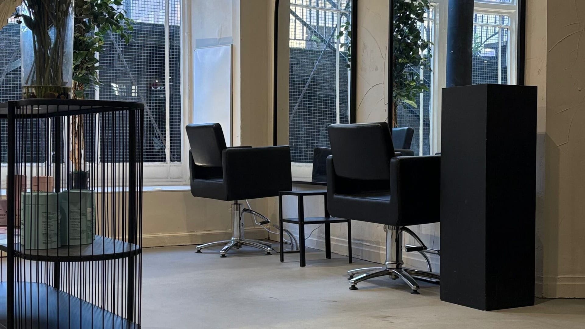 Modern salon interior at The Collective Hair Co, Glasgow, Scotland, GB with sleek black chairs and large windows.