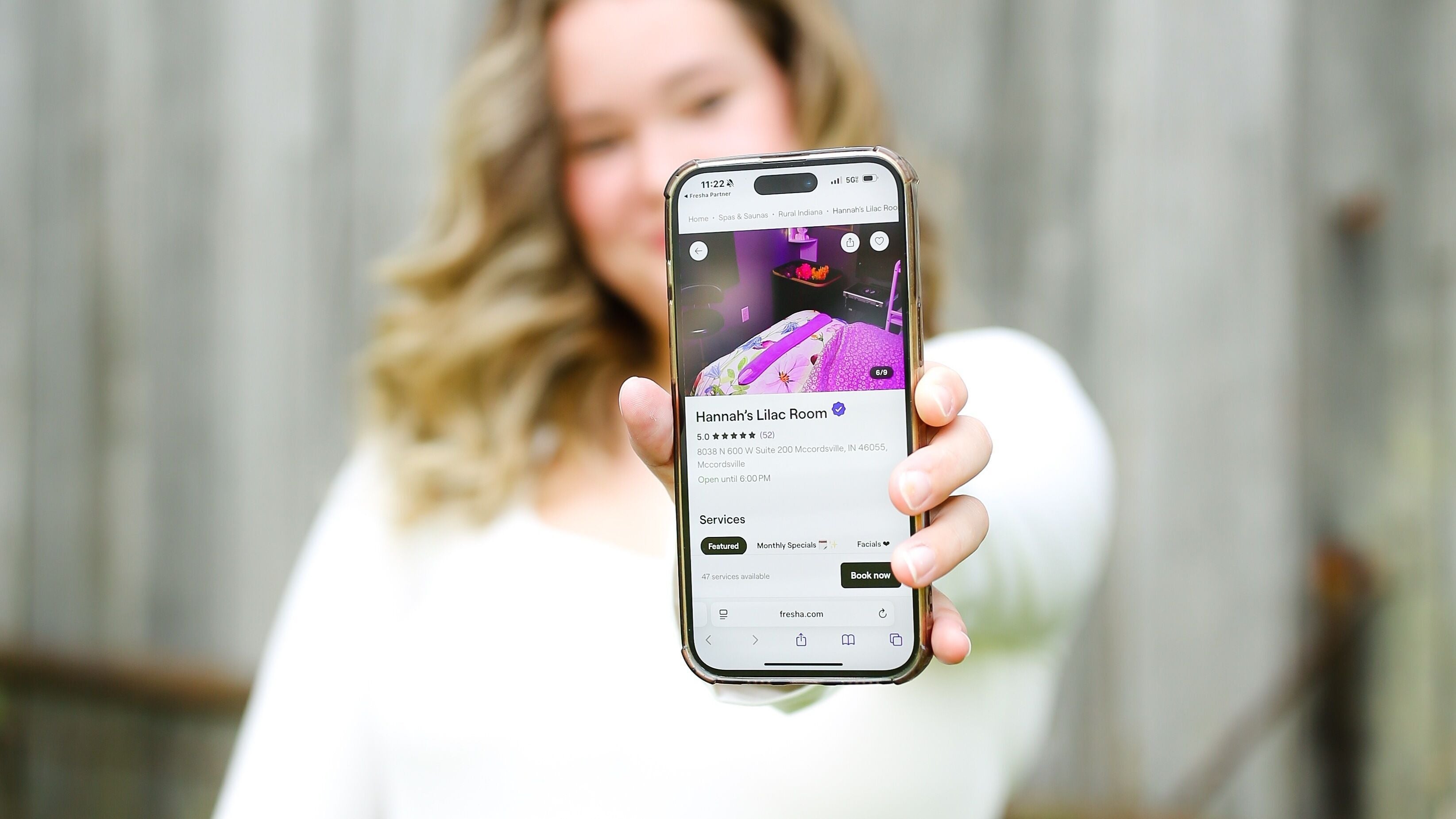 Woman showcasing Hannah’s Lilac Room booking page on phone in Mccordsville, Indiana, US.