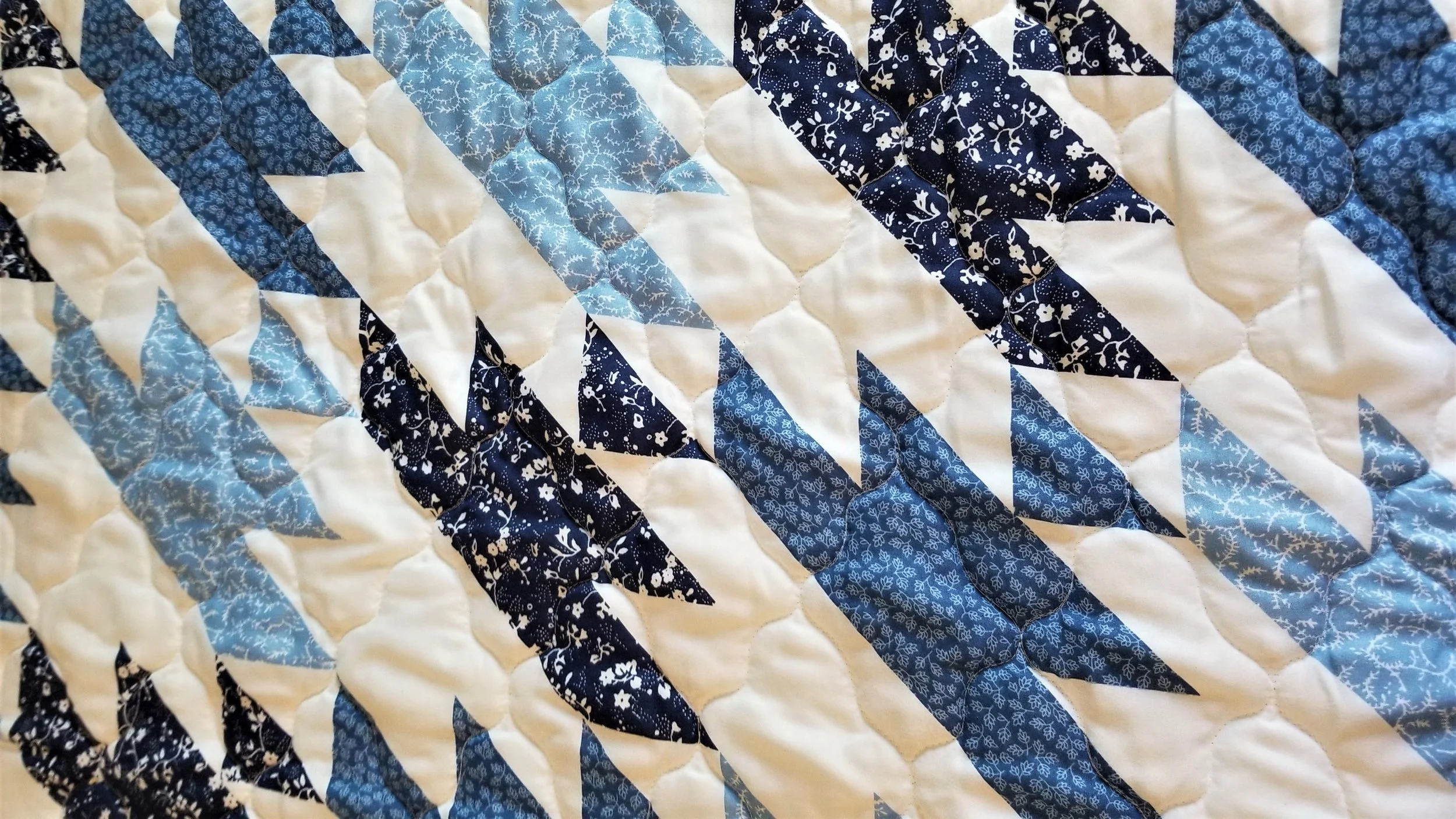 Close-up of a quilt with a pattern of blue, white, and dark blue fabrics in leaf and geometric shapes.