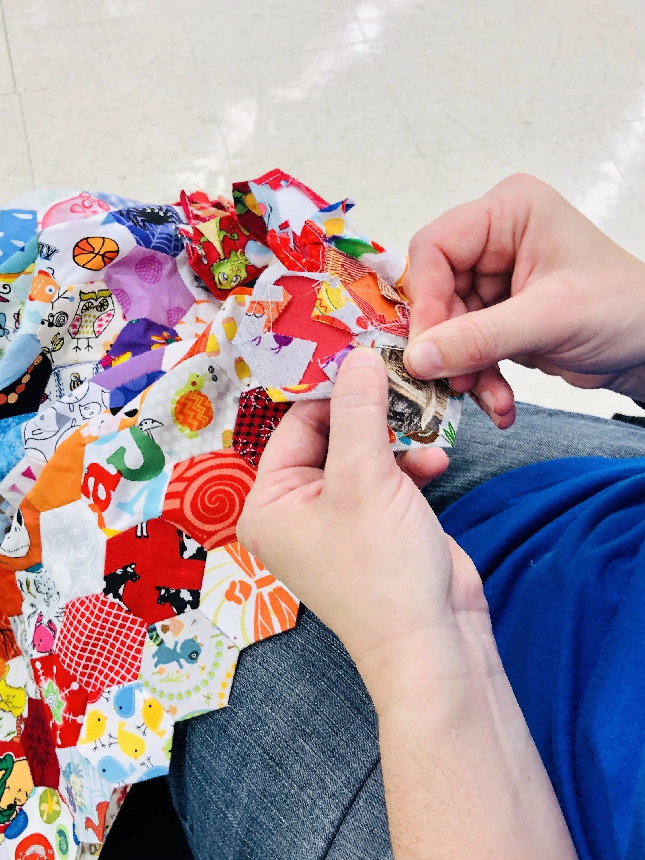 Person sewing a colorful patchwork quilt with various fabric patterns and designs.