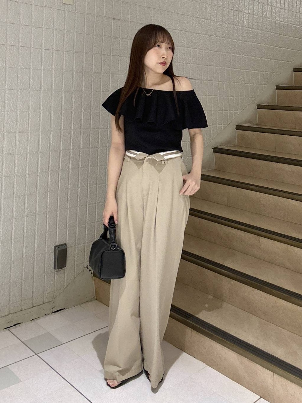 ベージュ系のチノパンツ、ブラック系のニット/セーター、ブラック系のショルダーバッグを着用したレディースの春コーディネートの1枚目の写真