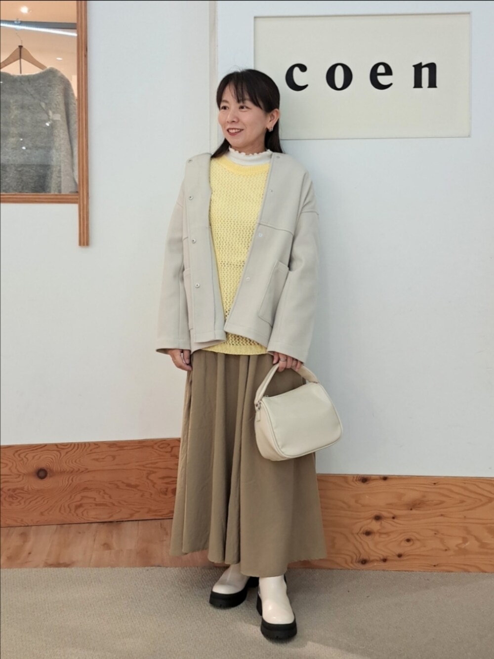 ホワイト系のTシャツ/カットソー、イエロー系のニット/セーター、グレー系のノーカラーコートを着用したレディースの秋コーディネートの1枚目の写真