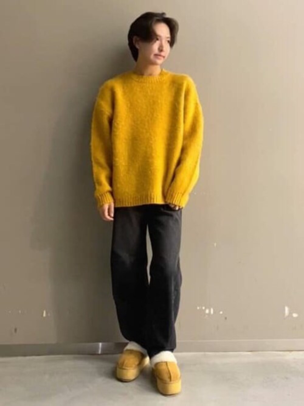 イエロー系のニット/セーター、ブラック系のデニムパンツ、ベージュ系のスリッポンを着用したメンズの秋コーディネートの1枚目の写真