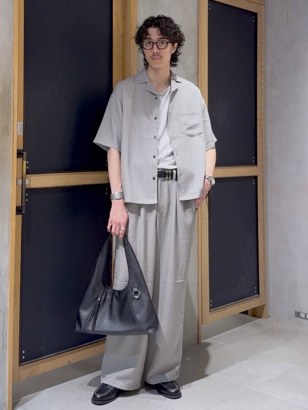 グレー系のスラックス、グレー系のシャツ/ブラウス、ブラック系のモカシン/デッキシューズを着用したメンズの春コーディネートの1枚目の写真