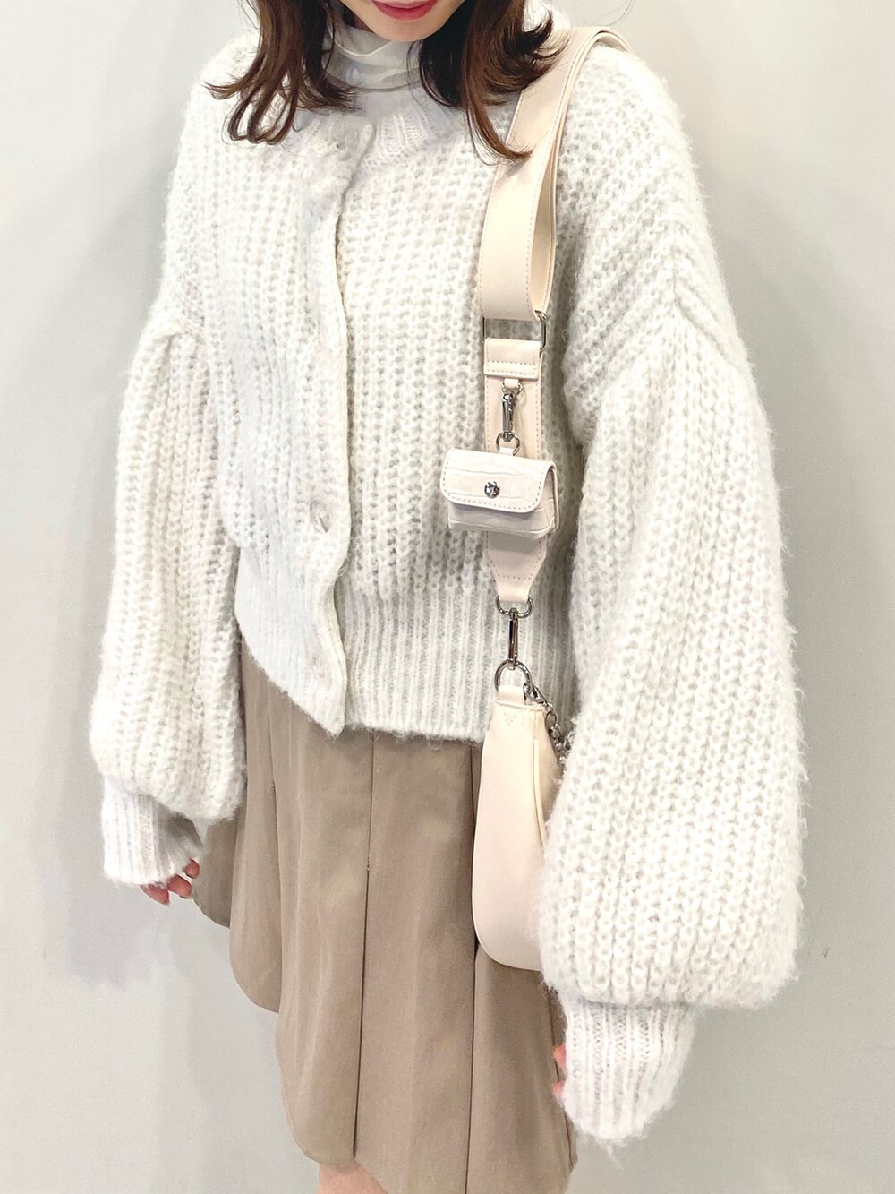 ホワイト系のショルダーバッグ、ホワイト系のカーディガン/ボレロ、ホワイト系のTシャツ/カットソーを着用したレディースの冬コーディネートの2枚目の写真
