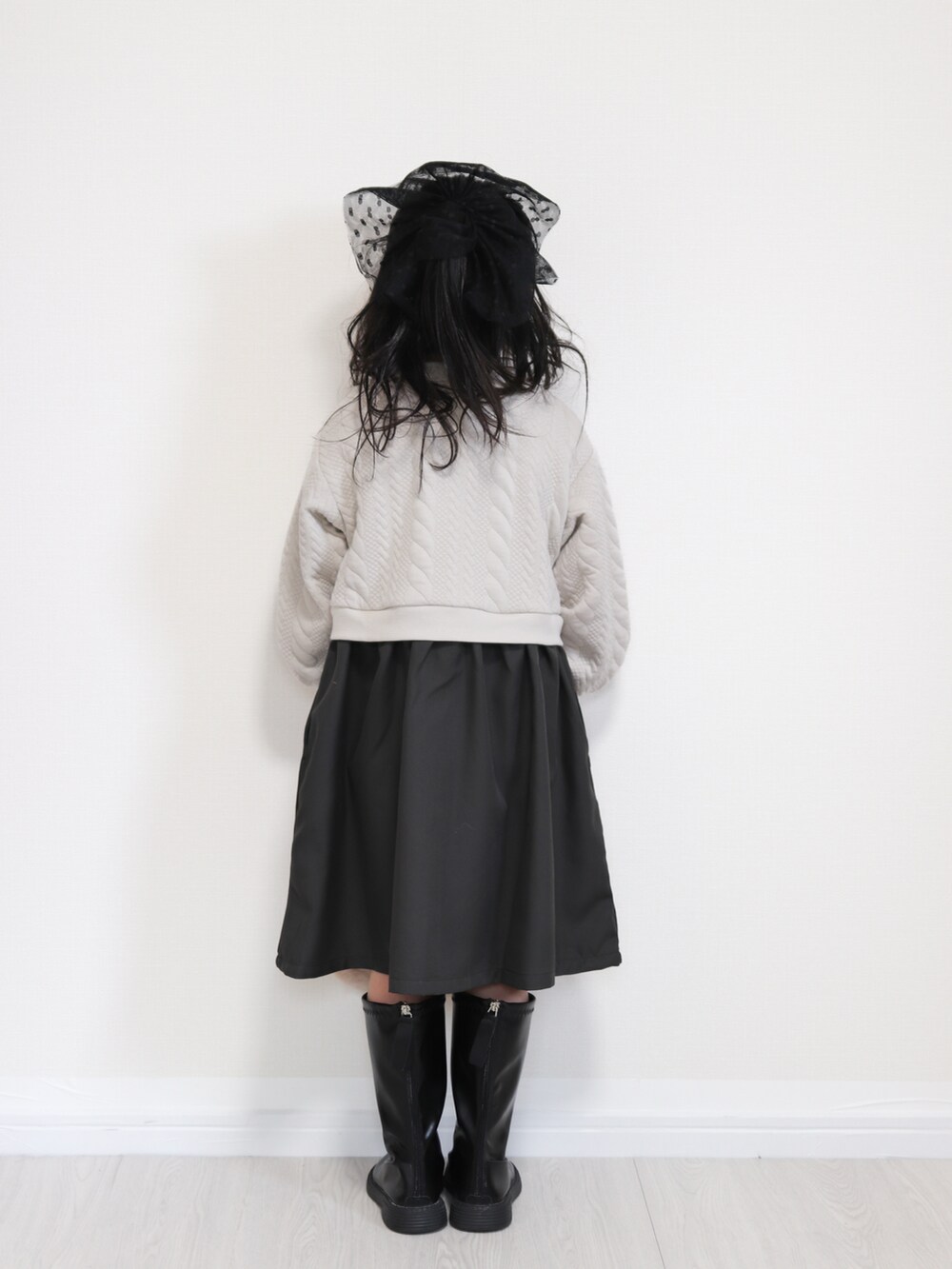 ベージュ系のワンピース、ベージュ系のハンドバッグ、ブラック系のブーツを着用したキッズの冬コーディネートの3枚目の写真