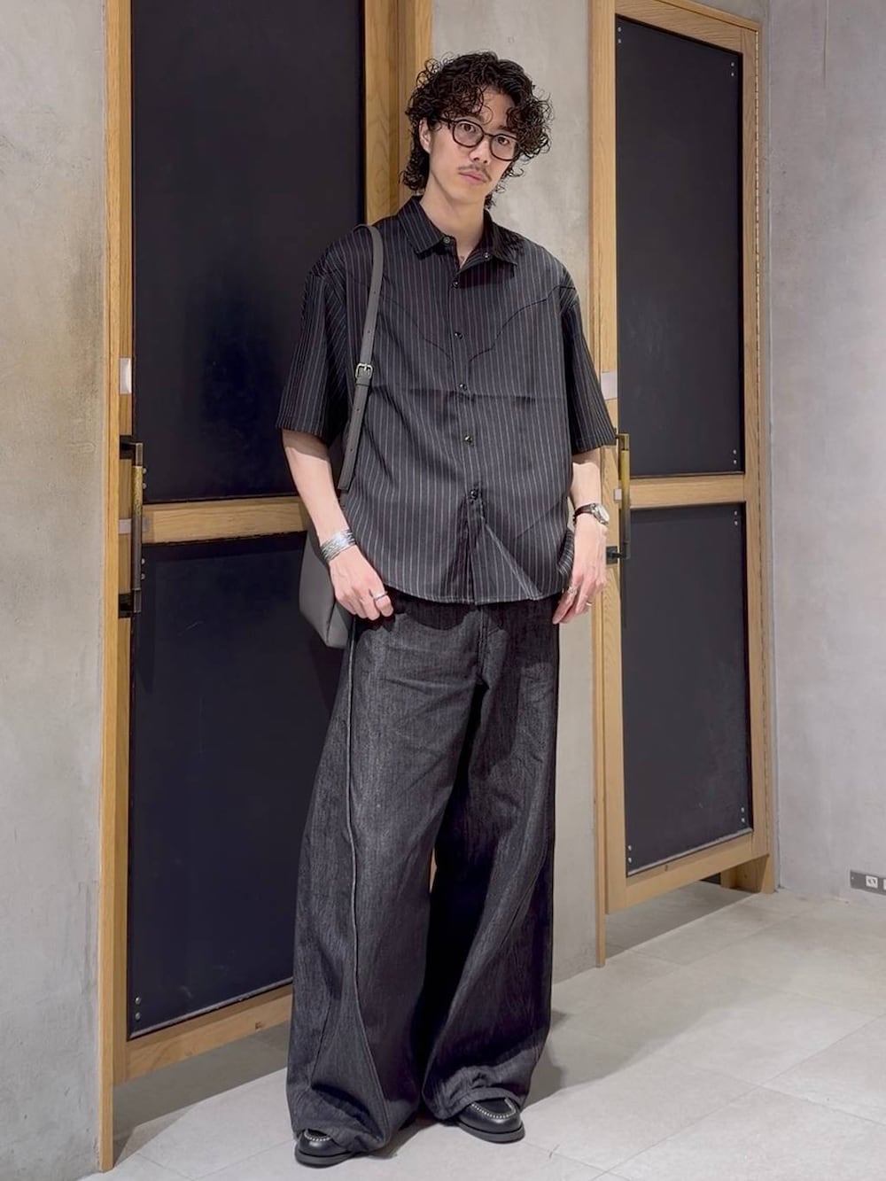 グレー系のショルダーバッグ、ブラック系のモカシン/デッキシューズ、ブラック系のデニムパンツを着用したメンズの夏コーディネートの3枚目の写真