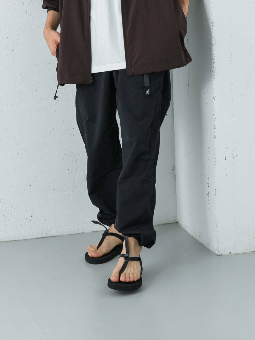 ブラック系のその他パンツ、ブラック系のサンダル、レッド系のナイロンジャケットを着用したメンズの夏コーディネートの3枚目の写真