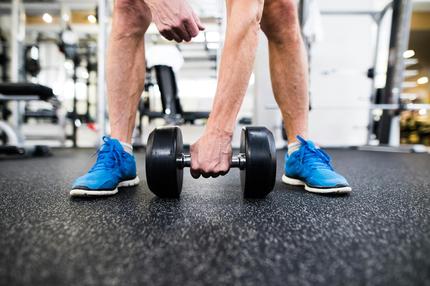 Sport im Alter: Symbolbild: Ein älterer Mann trainiert im Fitness Studio mit einer Hantel.
