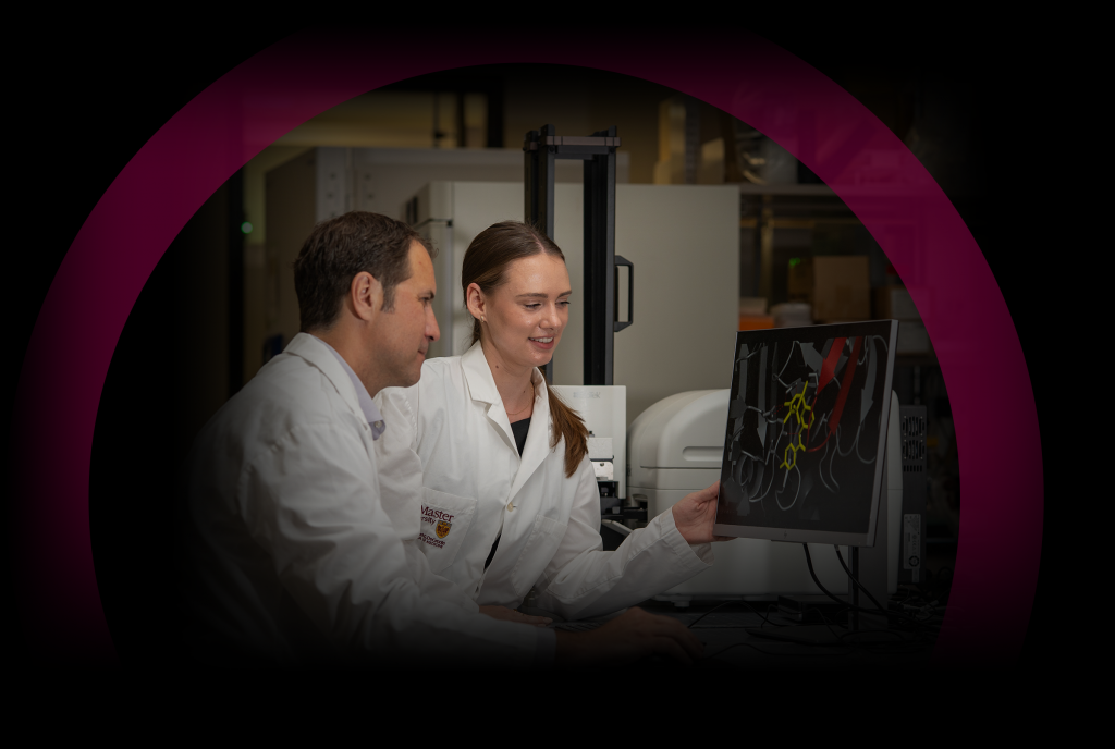 McMaster researchers in lab coats looking at a computer monitor