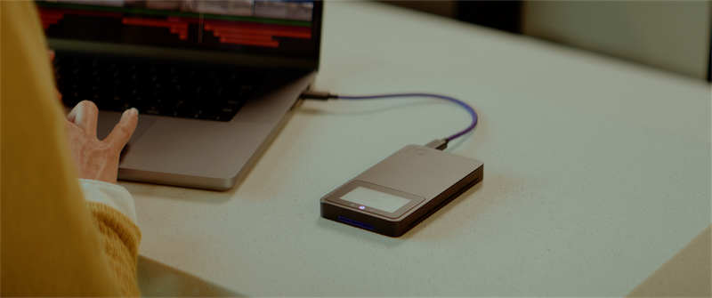 Person editing video on a laptop with iodyne Pro Mini portable SSD connected via USB-C, showcasing its sleek design and Digital Label feature.