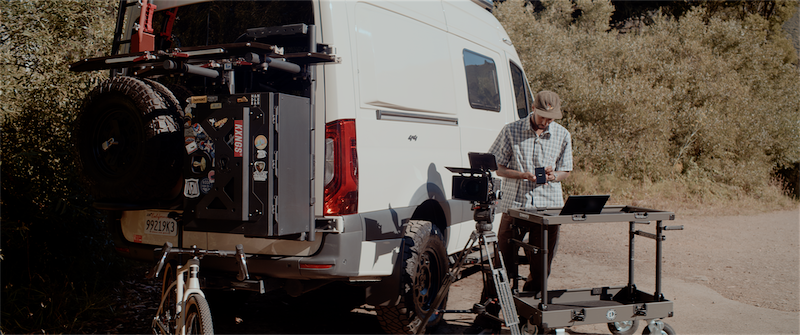 Man working on a laptop near a van equipped for outdoor filming, showcasing a portable setup ideal for professional creatives using iodyne Pro Mini SSD for data storage.