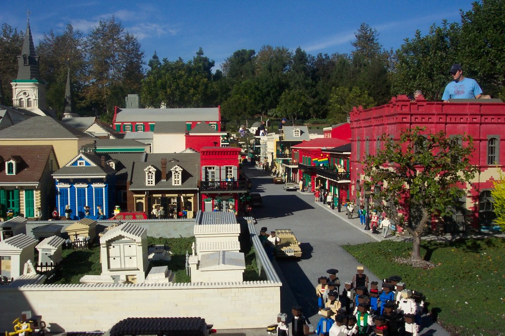 There are several buildings made by Lego blocks and in the background, there are people looking at the buildings.