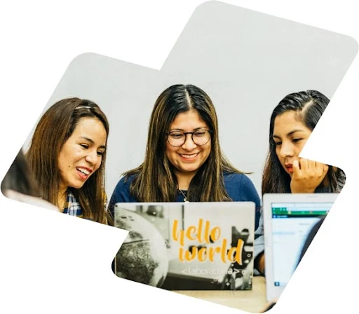 Three young women sit together at desk and look at laptop