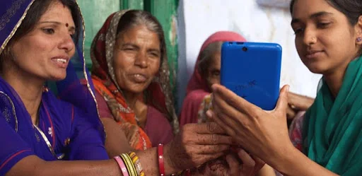 Four Indian women in traditional Indian clothing look at smartphone together