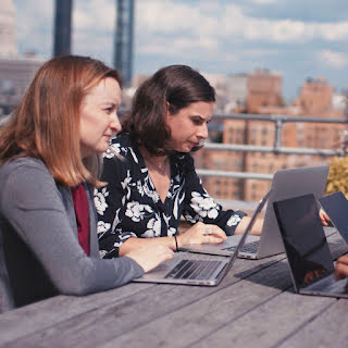 Dos mujeres trabajando en sus laptops en una terraza junto con otras dos personas que están fuera de encuadre.