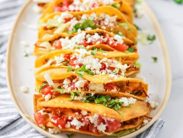 Chicken Tacos stacked on white platter with dish cloth.