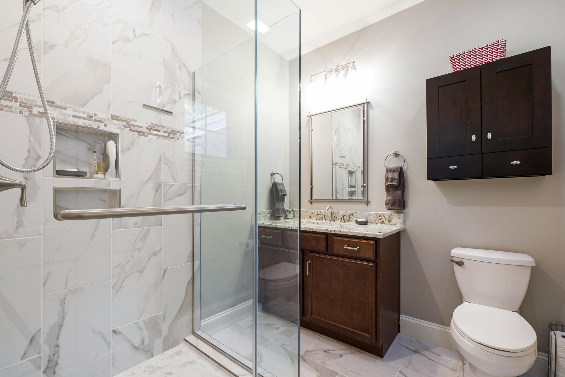 A modern bathroom featuring a glass-enclosed shower with marble tiles, a dark wood vanity, and a white toilet.