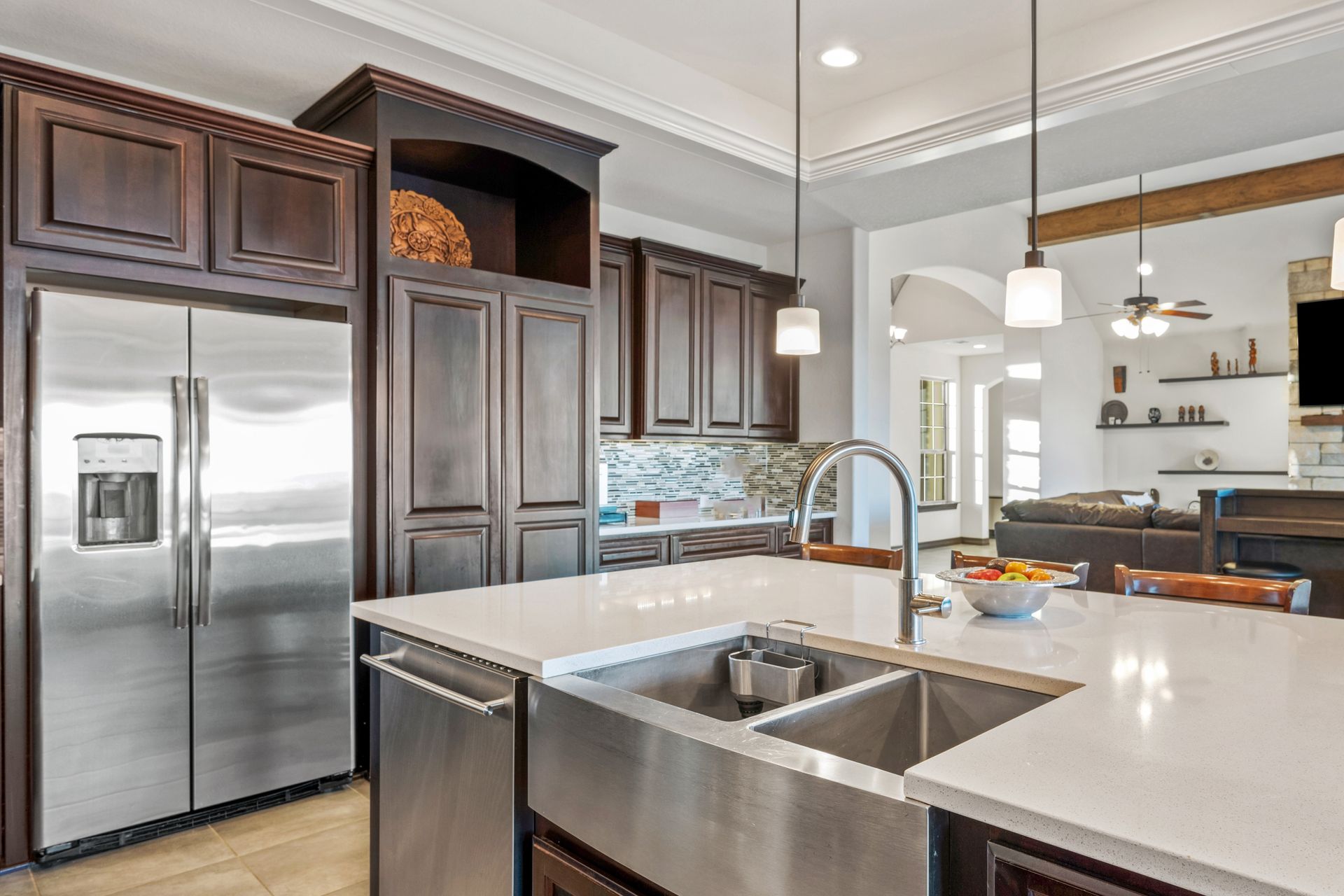 A modern kitchen features dark wood cabinetry, a stainless steel farmhouse sink, and a large white island countertop.