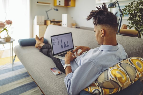 Person lying on couch with laptop screen showing charts.