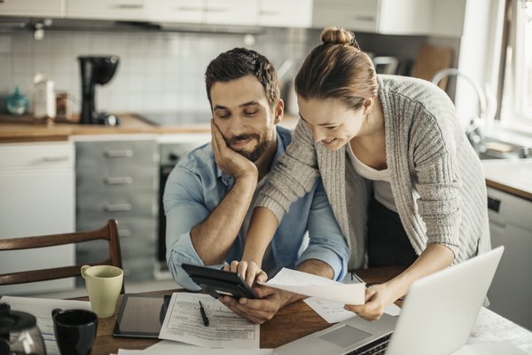 Two smiling people review paperwork at home in front of laptop.