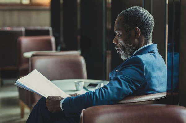 Businessman wearing suit and tie sitting at coffee shop and reading daily newspaper.