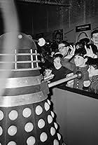 British actress Carole Ann Ford (centre, right) makes a horn sign at a Dalek from the BBC television science fiction series 'Doctor Who', at the Daily Mail Schoolboys' and Girls' Exhibition at Olympia, London, 28th December 1964. In the series, Ford plays Susan Foreman, the companion of the first Doctor, played by William Hartnell.