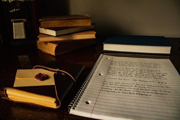 Desk with an open notebook with writing, old books stacked to the side Desk with an open notebook with writing, old books stacked to the side