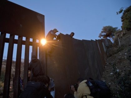 A Honduran migrant helps other immigrants cross to the U.S. side of the border wall, in Ti