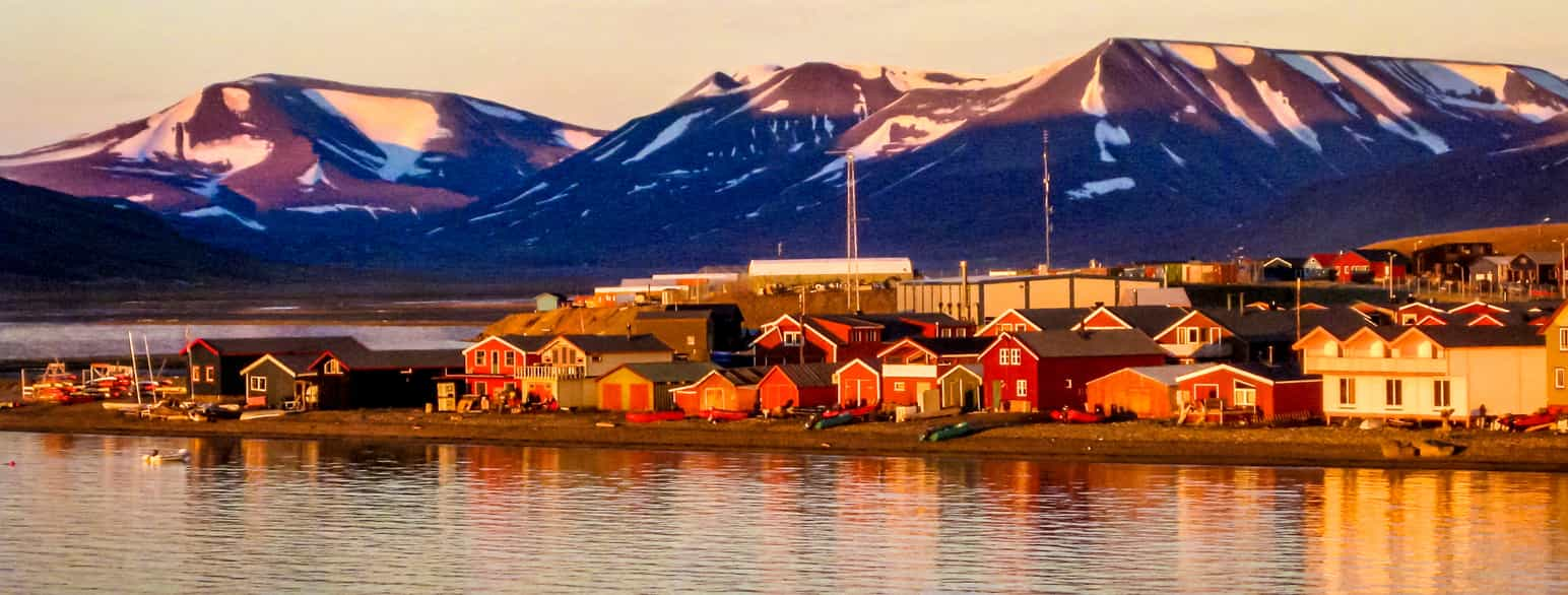 foto av hus ved sjøen nedenfor et fjell i sol