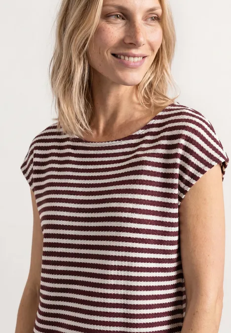 Gebreide jurk rustic rouge Een persoon met halflang blond haar draagt een T-shirt met korte mouwen en bruin-witte strepen.