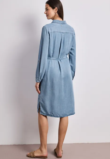 Knielange jurk in een verwassen look Light Blue soft wash Vrouw van achteren in een knielange spijkerjurk met lange mouwen, blootsvoets.