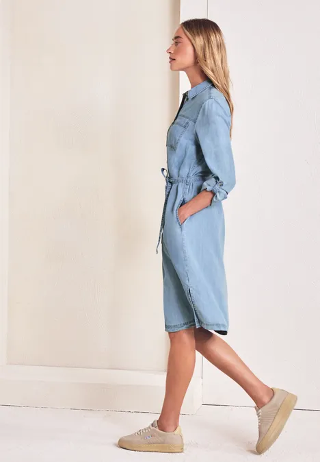 Knielange jurk in een verwassen look Light Blue soft wash Zijaanzicht van een vrouw in een lichtblauwe denim jumpsuit met ceintuur en plateauzolen.