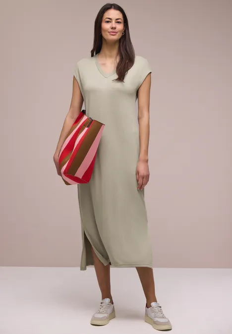 Midi-jurk met V-hals in een gebreide look timeless beige Vrouw in mouwloze midi-jurk licht beige, witte sneakers en gestreepte schoudertas.