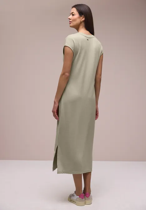 Midi-jurk met V-hals in een gebreide look timeless beige Vrouw van achteren in lichtgroene midi-jurk met korte mouwen, zijslitsen en gebloemde sneakers.