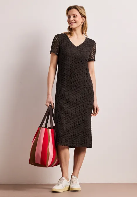 Kanten midi-jurk in effen kleur espresso brown Vrouw in zwarte midi-jurk met stippen, witte sneakers, met een rode gestreepte shopper.