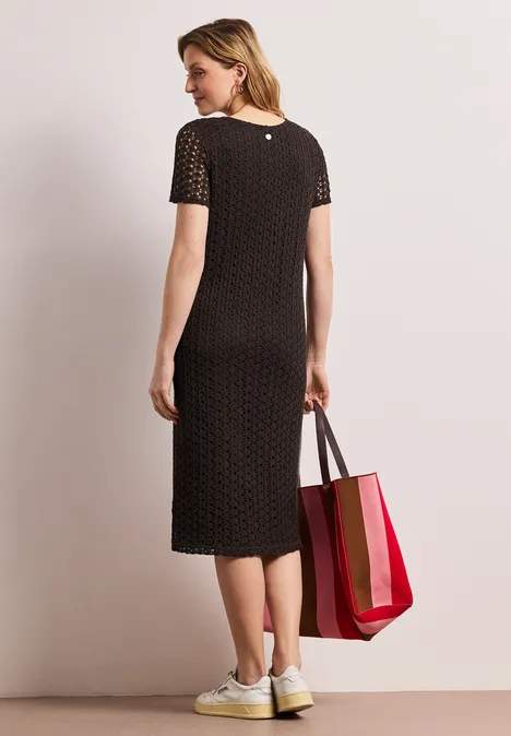 Kanten midi-jurk in effen kleur espresso brown Een vrouw van achteren in een zwarte midi-jurk met stippen, witte sneakers en een rood-roze tas.