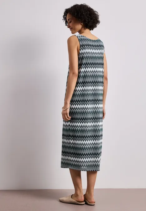 Midi-jurk met V-hals in jacquardstof deep bound green Vrouw in maxi jurk met zigzagpatroon en sandalen, staand voor een effen achtergrond.
