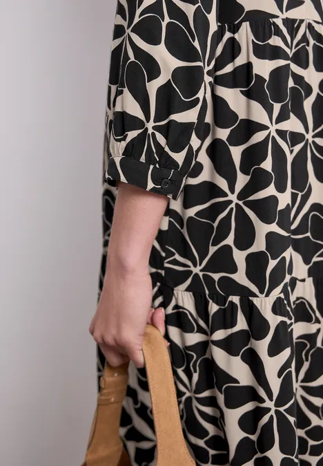 Midi-jurk met gespleten hals in etnische look Black Persoon in zwart-witte jurk met motief houdt een bruine handtas vast.