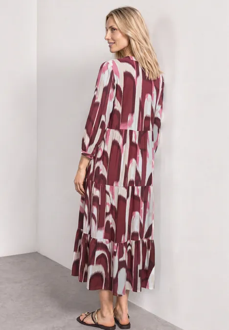 Midi-jurk met gespleten hals in etnische look rustic rouge Vrouw in zijaanzicht draagt een midi-jurk met rood-witte geometrische print tegen een neutrale achtergrond.