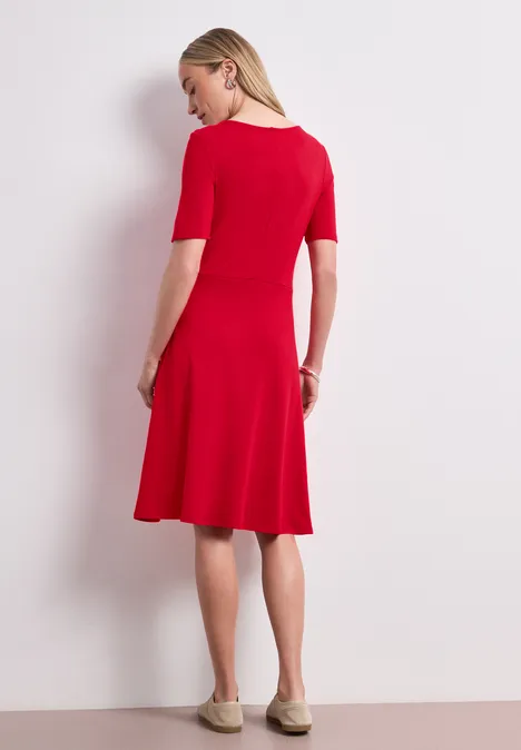 Knielange jersey jurk met korte mouwen salsa red Een vrouw in een rood, knielang jurkje met driekwartmouwen, zijdelings vanaf achteren.